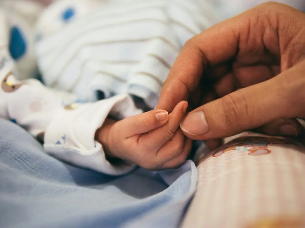 close-up of baby and adult holding hands depicting The First 40 Days: An Alternative Model for Postpartum Recovery