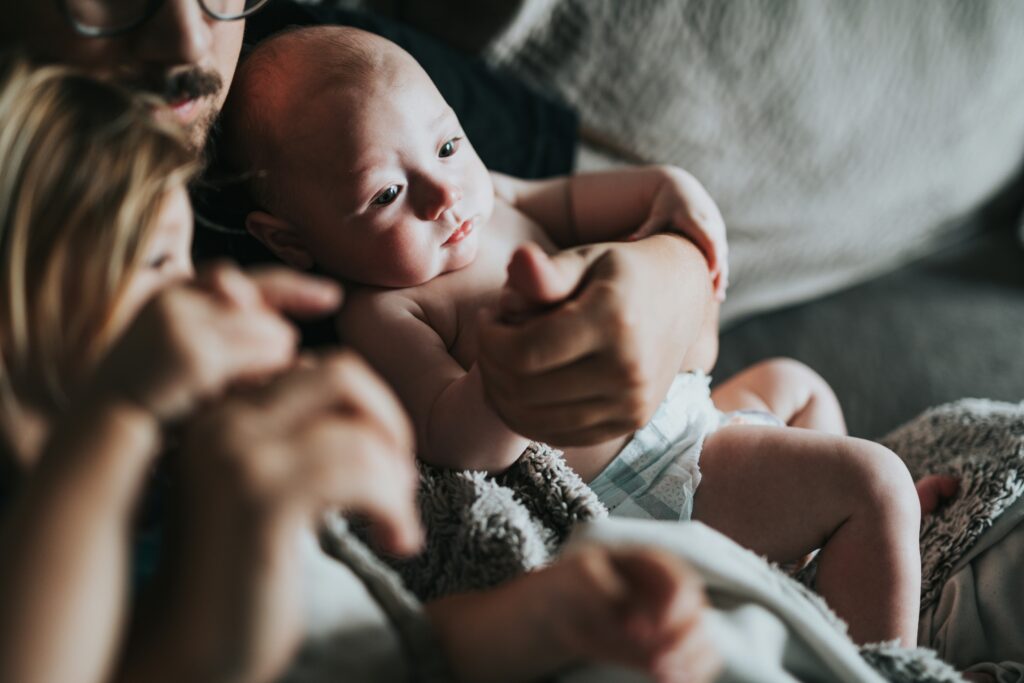 infant being held by man around family depicting What We Can Learn From the First 40 Days of postpartum